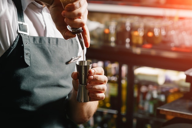 Manos masculinas del barman, hace un cóctel en el bar, vasos con hielo.