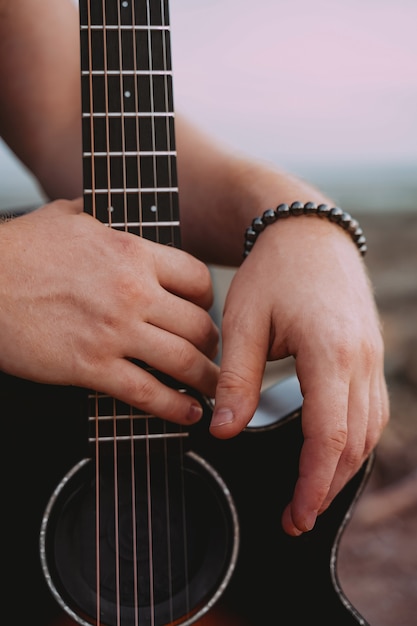 Manos masculinas cerca de la guitarra acústica negra. Exterior