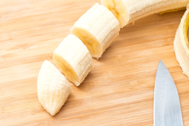 Manos masculinas cortando plátano en el tablero de la cocina. De cerca. Enfoque selectivo.