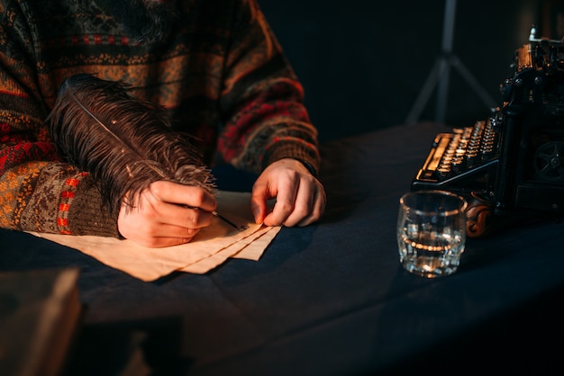 Manos masculinas escribe con una pluma sobre papel vintage