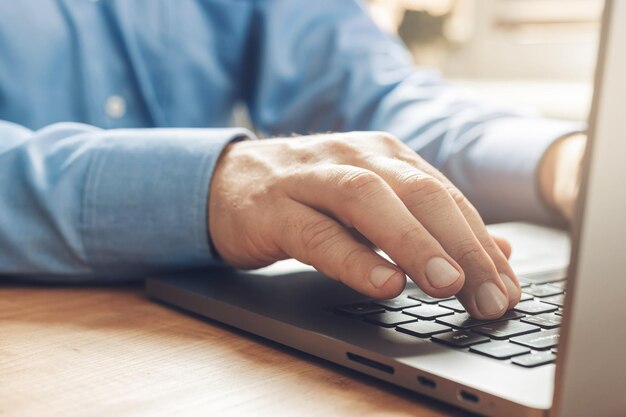 Manos masculinas escribiendo en un teclado de computadora portátil, vista cercana