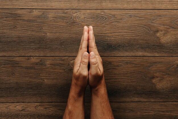 Foto manos masculinas están plegadas en oración sobre una mesa de madera