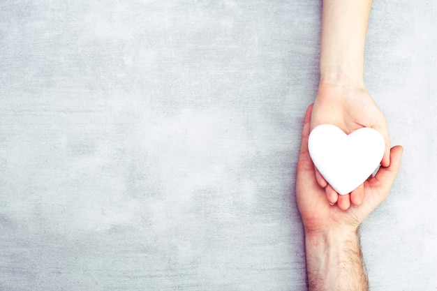 Manos masculinas y femeninas con un corazón blanco, cuidado de la salud, amor y concepto de seguro familiar