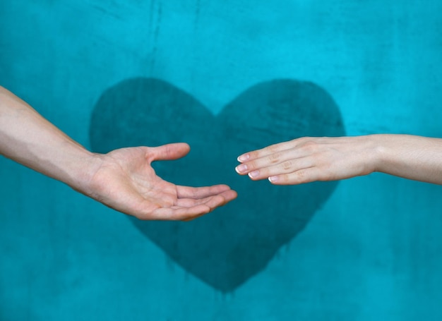 Manos masculinas y femeninas se extienden frente al corazón pintado en la pared