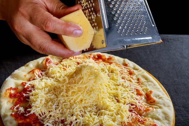 Las manos masculinas frotaban el queso rallado en la pizza