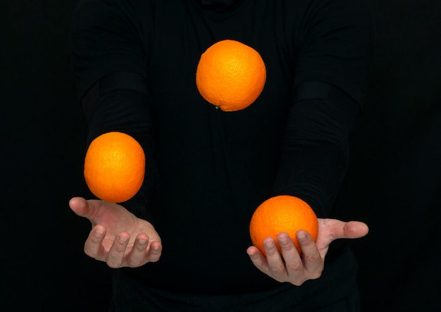 Las manos masculinas hacen malabarismos con naranjas frescas en una pared oscura