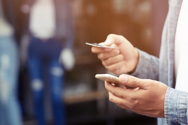 Manos masculinas jóvenes con tarjeta de crédito y uso de teléfonos móviles inteligentes