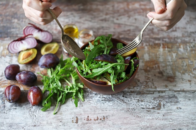 Las manos masculinas mezclan ensalada en un tazón con cuchara y tenedor.