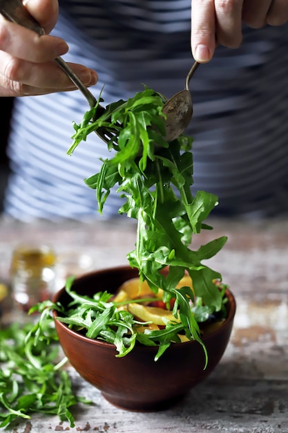 Las manos masculinas mezclan ensalada en un tazón con cuchara y tenedor.