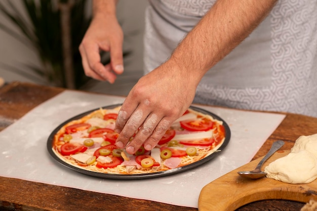 manos masculinas poniendo comida en la pizza