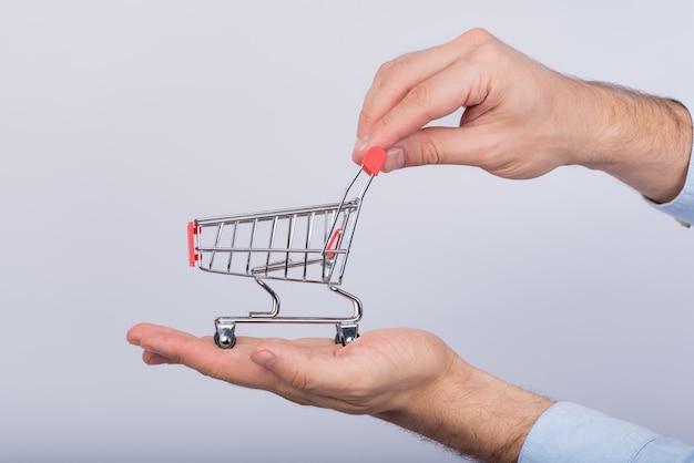 Manos masculinas que sostienen el carro de compras pequeño en blanco. Vista lateral