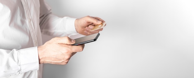 Manos masculinas que sostienen el teléfono móvil y la tarjeta de plástico, ingresan datos en la aplicación bancaria para pagar en línea.