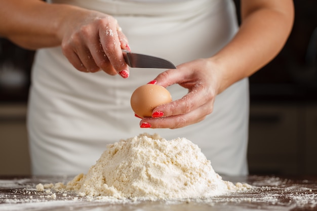 Manos masculinas rompen el huevo en harina para pasta en la mesa de la cocina de madera vieja.