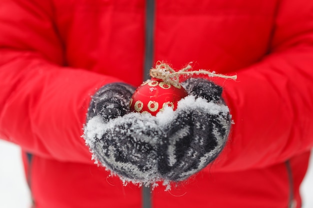 manos masculinas sosteniendo una bola de Navidad roja. Frosty día de invierno en bosque nevado. Tema Feliz Navidad y Feliz Año Nuevo