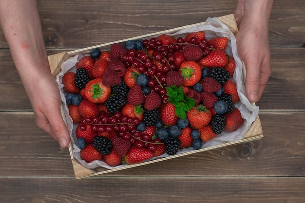 Manos masculinas sosteniendo una caja de madera con bayas frescas en la mesa de madera vintage. Moras frecas.