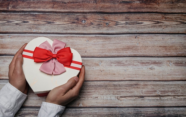 Manos masculinas sosteniendo una caja de regalo en forma de corazón con pajaritas. Tema de San Valentín. Concepto LGTBI