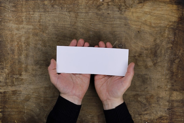 Manos masculinas sosteniendo una hoja de papel en blanco en el fondo de la tabla de textura de madera