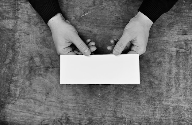 Manos masculinas sosteniendo una hoja de papel en blanco en el fondo de la tabla de textura de madera