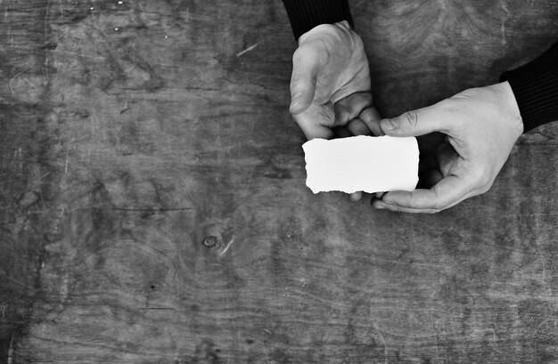 Manos masculinas sosteniendo una hoja de papel en blanco en el fondo de la tabla de textura de madera