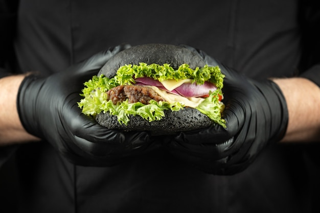 Manos masculinas sosteniendo hombre de hamburguesa de carne negra deliciosa fresca en el uniforme de chef negro