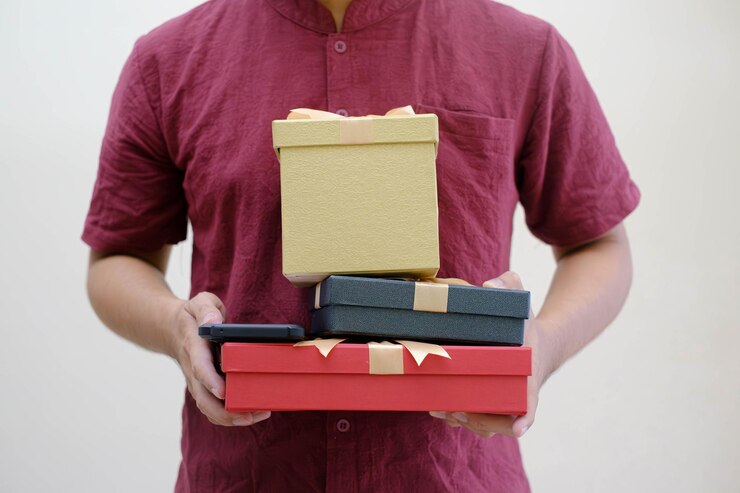 Manos masculinas sosteniendo pequeñas cajas de regalos envueltas con cinta de oro en un fondo blanco aislado