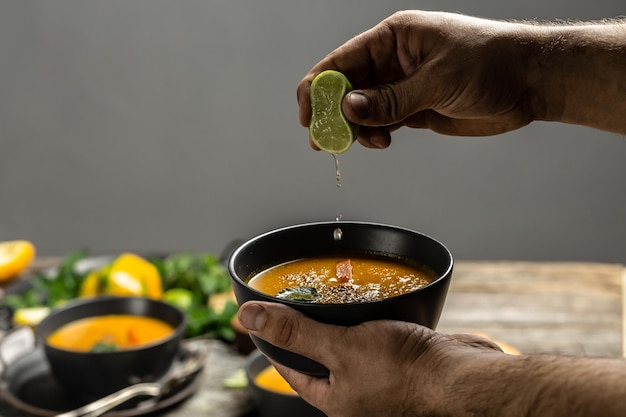 Manos masculinas sosteniendo un plato de sopa de calabaza Plato de sopa casera de zanahoria y cilantro con pimientos horneados y queso jugo de lima y jengibre