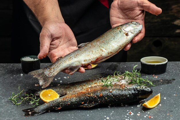 Manos masculinas sosteniendo trucha arco iris con especias Cocina de platos de pescado Concepto de panadería de cocina culinaria
