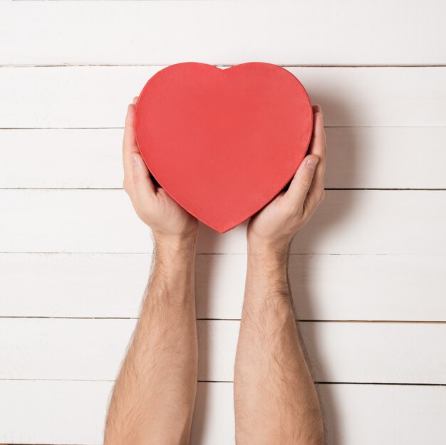 Manos masculinas sostienen una caja roja en forma de corazón