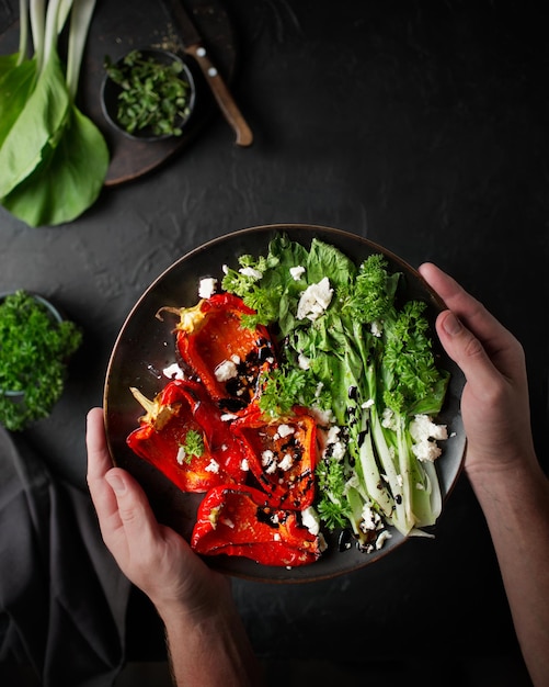 Manos masculinas sostienen un plato de comida Ensalada con pimienta al horno, queso feta y pak choi Chef está cocinando