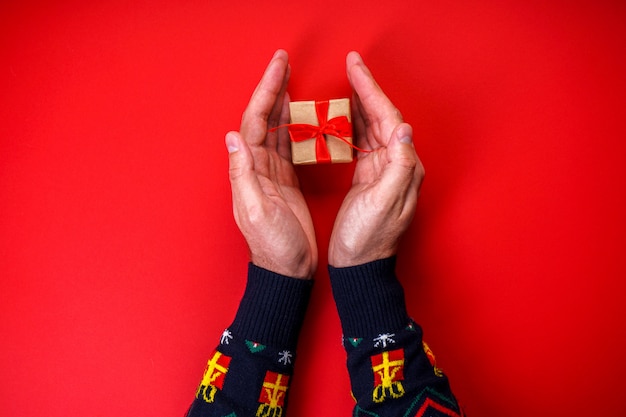 Manos masculinas en un suéter de Navidad con un regalo en rojo.