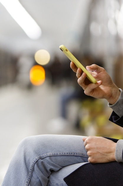 Foto manos masculinas con teléfono celular / teléfono inteligente en caja amarilla en la plataforma de la estación de metro