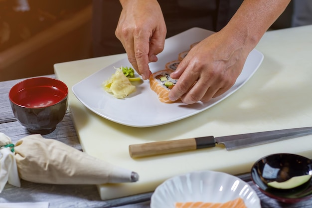 Manos masculinas tocan rollos de sushi. Sushi y wasabi en un plato. Nueva receta de comida japonesa. Rollos de uramaki con pescado.