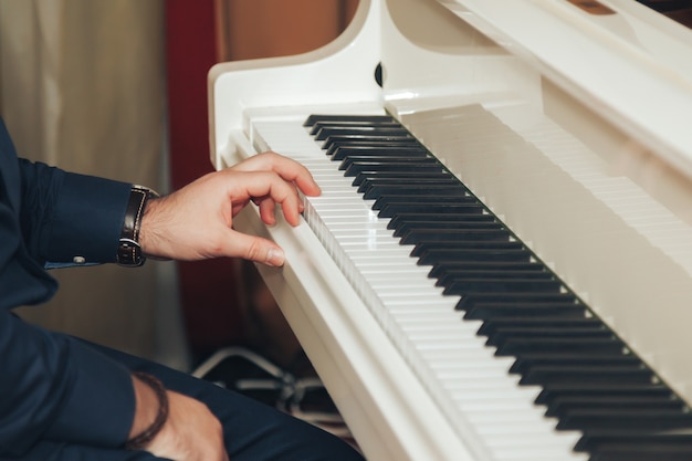 Manos masculinas tocar el piano blanco en la habitación