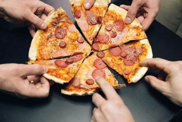 Manos masculinas tomando rebanadas de pizza con tomates con queso y jamón del grupo de entrega de alimentos de hambrientos