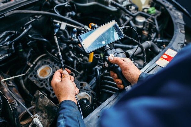 Manos de mecánico de automóviles revisan el motor del vehículo con endoscopio técnico con cámara giratoria