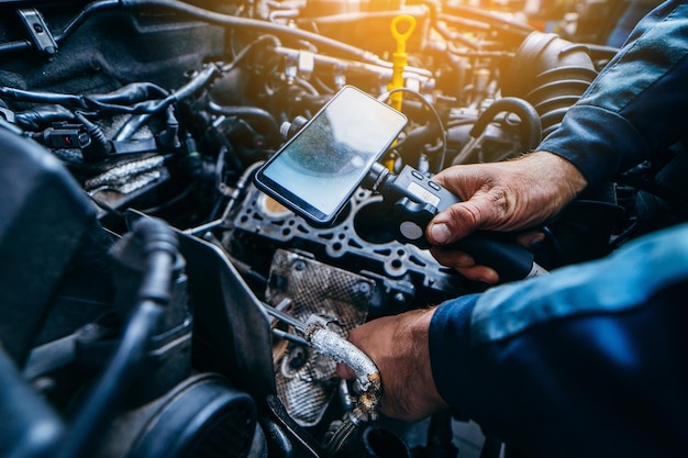 Manos de mecánico de automóviles revisan el motor del vehículo con endoscopio técnico con cámara giratoria