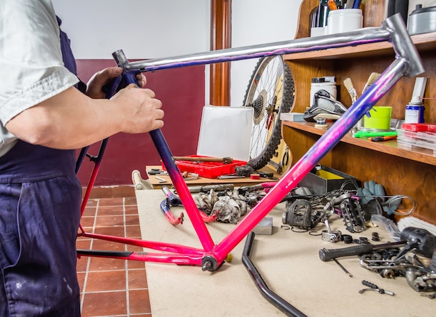 Manos de mecánico de bicicletas reales limpieza de bicicleta de cuadro dañado en un taller