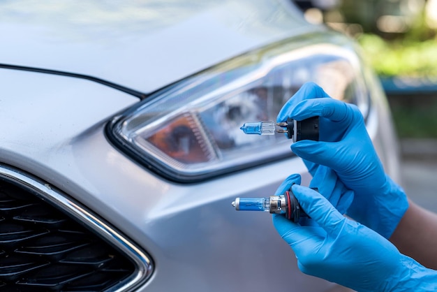 Manos de un mecánico fuerte sostienen lámparas halógenas de automóviles contra faros y reparan automóviles