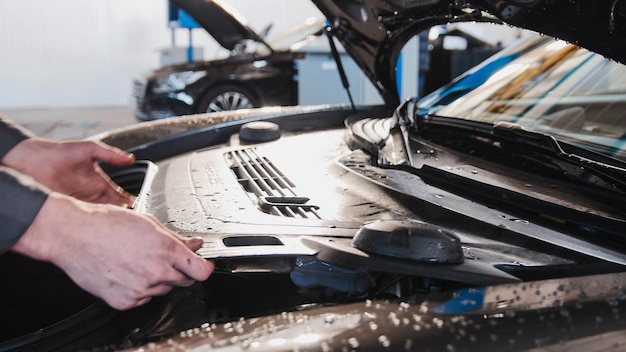 Manos del mecánico en el garaje de automóviles control del capó del coche de lujo