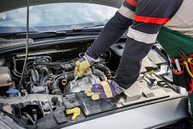 Manos del mecánico en guantes protectores con motor de coche de cerca