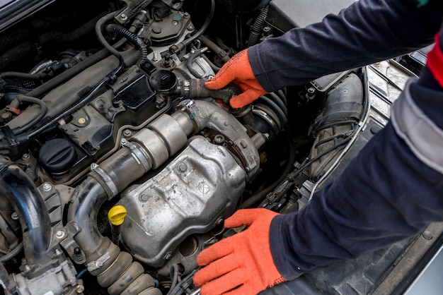 Manos del mecánico en guantes protectores con motor de coche de cerca