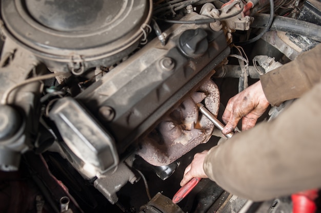 Manos de mecánico reparador trabajando en motor usando herramienta