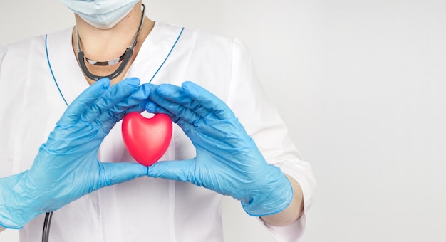 Manos de médico cardiólogo con corazón. Vista cercana del corazón en las manos con guantes de médico con bata blanca.