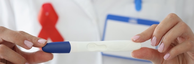 Las manos del médico con cinta roja en el pecho sostienen la prueba de embarazo closeup