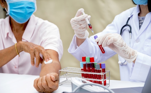 Foto manos de un médico con una jeringa y una muestra de tubo de sangre para el análisis del paciente mayor