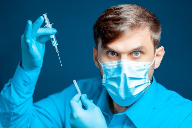 En manos de un médico, un médico con una máscara médica y guantes, vestido con un uniforme azul, una jeringa de inyección