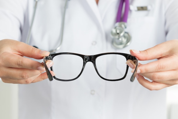 Foto las manos del médico oculista femenino dando un par de gafas negras. buen concepto de visión