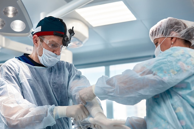 Manos de médicos con guantes durante una operación, primer plano de una enfermera operativa que ayuda a un cirujano a ponerse guantes de styryl antes de la operación.