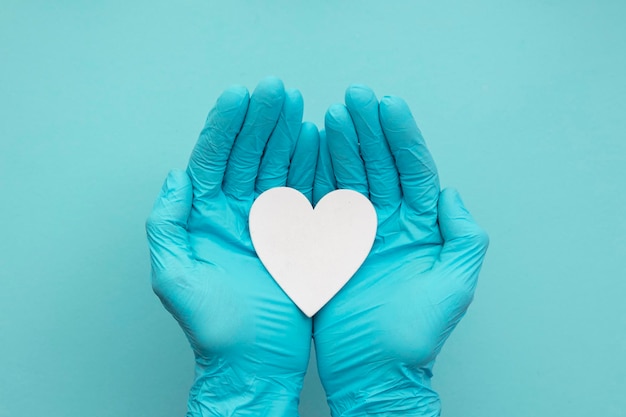 Manos de los médicos con guantes quirúrgicos azules con forma de corazón blanco