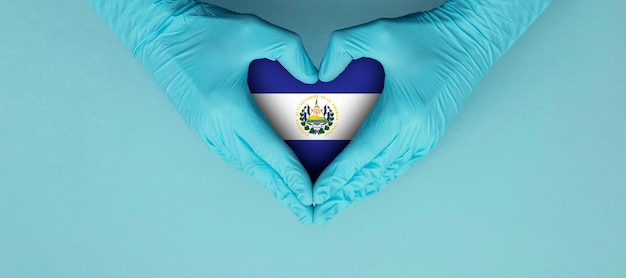 Manos de los médicos con guantes quirúrgicos azules que hacen oír el símbolo de forma con la bandera de el salvador